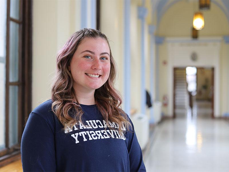 Woman in college hallway, wearing Immaculata sweatshirt